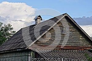 Old gray wooden attic of a rural house with a small window under a  slate roof