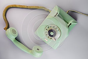 Old green antique rotary telephone with removed receiver on blue background. Vintage landline home phone with dial