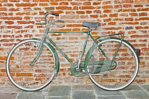 Old green bicycle parked against a brick wall