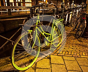 Old green bicycle parked near bridge in Amsterdam at night.