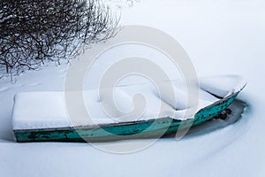 An old green boat in a frozen lake. Boat covered with pure snow