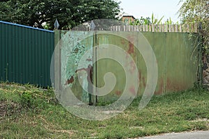 Old green metal old gate in brown rust and a closed door on an iron fence