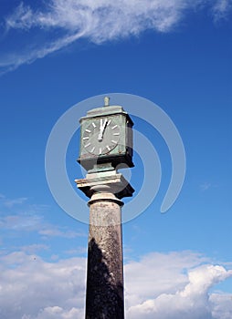 Old green metal outdoor clock on a stone pillar in arnside cumbria against a blue cloudy sky