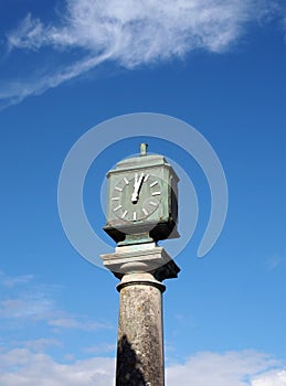 Old green metal outdoor clock on a stone pillar in arnside cumbria against a blue cloudy sky