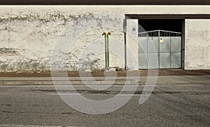 Old green pole on sidewalk with metal gate on the left and grunge white plaster wall on behind. Urban street in front