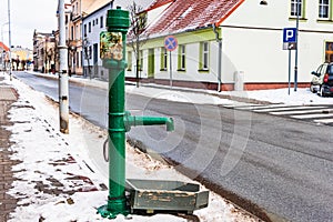 Old green street water pump.In the background street and buildings painted in different colors