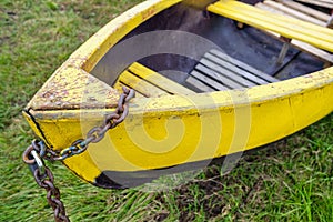 An old green wooden boat chained up on the lake shore in summertime