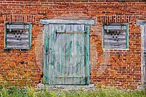 Old green wooden cracked door and windows on a retro red brick wall facade