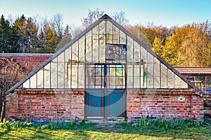 Old greenhouse with brick wall and glass panes. The entrance is an antique old door