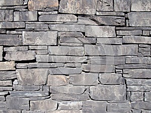 Old grey slate stone wall with irregular shaped slabs