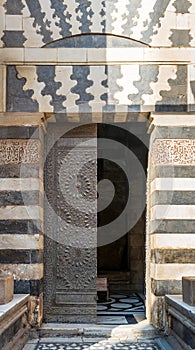 Old grunge decorated bronze-plate door surrounded by striped black and white marble decorations