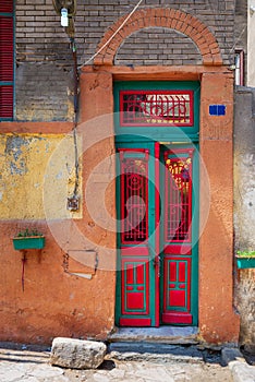 Old grunge decorated door painted in green and red vibrant colors on orange painted stone wall