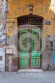Old grunge green decorated painted door on dirty yellow painted stone wall