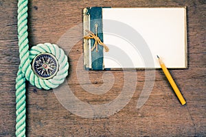 Old grunge notebook, vintage compass, pencil, rope on wooden table background