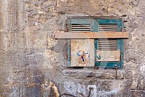 Old grunge window with closed green broken shutters on dirty bricks stone wall