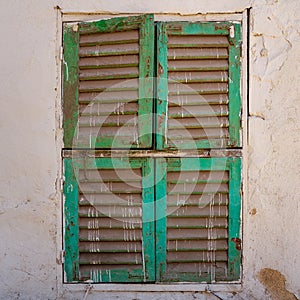 Old grunge window with closed green shutters on dirty bricks stone wall