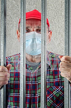 Old guy in a red cap looking through jail bars.