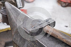 Old hammer lies on large metal anvil in farriery workshop