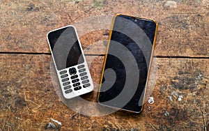 old hand phone with keypad and touchscreen smartphone on wooden table