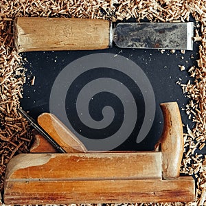 Old hand plane and chisel with wooden shavings on black background. Old woodworking hand tool. Top view. Copy, empty space for