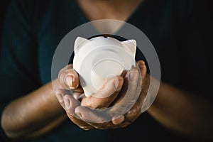 Old hands holding white piggy bank on darkness