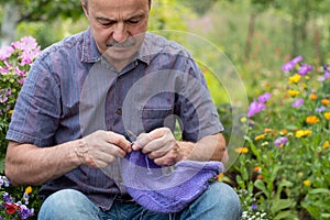 Old handsome man sitting at his summer garden with the knitting needles.