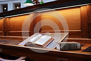 old hard cover book sitting at an old traditional timber reading desk under a glass lamp in an old state library in Melbourne,