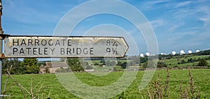 Old Harrogate and Pateley Bridge signpost with Menwith Hill Golf Balls in the background, North Yorkshire, England