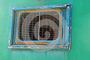 Old hatch window with rusty grille on the green wall
