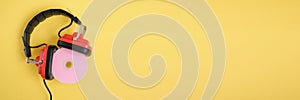 old headphones and pink cd disk on yellow background copy space