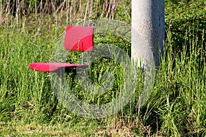 Old heavily used office chair with dilapidated red fabric left in family house backyard next to concrete utility pole