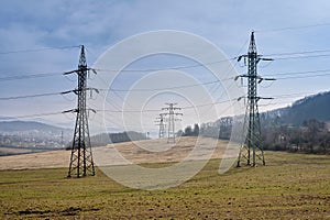 Old high-voltage power grid metal pylons supplying electricity to a small town in highlands in scenic landscape park