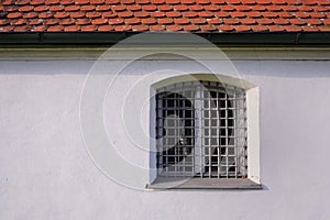 Old historic white plastered and weathered facade with a window and a grid of iron in front of red roof as background in Bavaria