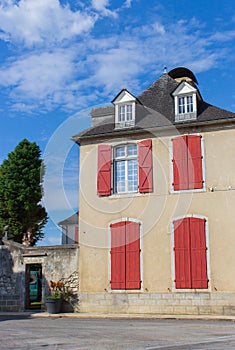 Old historical building with red window shutters and outdoor decor. Empty street in village, France. Facade of ancient house.