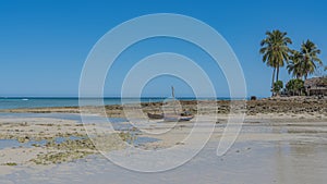 Old homemade wooden boats with masts stand on the sand at low tide.