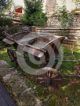 Old horse cart made of brown wood and rusty iron. Traditional moldovan rural transport. Wooden fence and wall of stone background