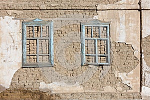 old house adobe air brick wall with two embedded wooden window frames and peeled off plaster leftovers - flat texture