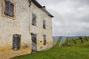 Old house with closed window shutters in french village. Ancient abandoned farm in mountains. Rural landscape.