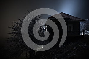 Old house with a Ghost in the forest at night or Abandoned Haunted Horror House in fog. Old mystic building in dead tree forest.