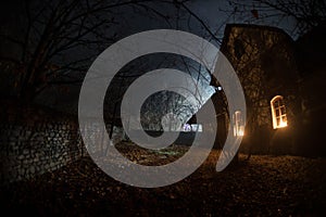 Old house with a Ghost in the forest at night or Abandoned Haunted Horror House in fog. Old mystic building in dead tree forest.