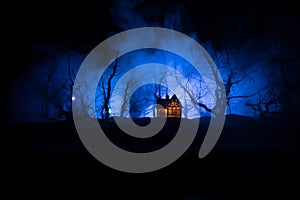 Old house with a Ghost in the forest at night or Abandoned Haunted Horror House in fog. Old mystic building in dead tree forest