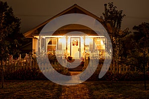 Old house at night with porch lights on and a picket fence at night