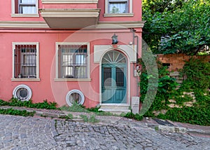 Old house painted in orange, wrought iron windows, and trees, at a cobblestone street, Balat district, Istanbul, Turkey