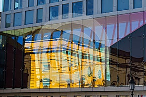 Old house reflected in glass windows of modern skyscraper.