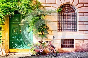 Old house wall in Trastevere, Rome, Italy with a red bicycle and green door. Old cozy street in Rome
