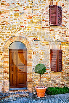 an old house with a wooden door and window shutter with a small tree in front