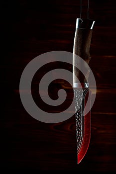 Old hunting knife hanging on the background of carved glowing red boards in the dark