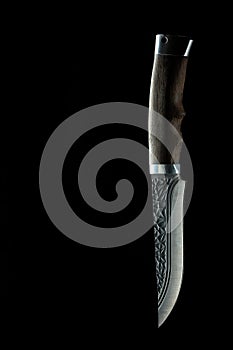 Old hunting knife lying on a carved wooden table in the dark