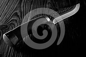 Old hunting knife lying on a carved wooden table in the dark