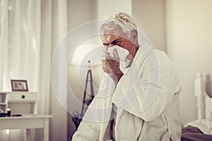 Old ill man blowing his nose using paper tissue